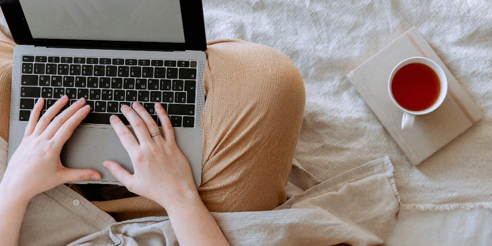 An employee using a laptop with an empty screen in bed while preparing to research how outsourcing promotes sustainability and impacts the economy.