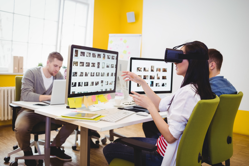 Young female executive enjoying augmented reality headset with colleagues sitting at creative office