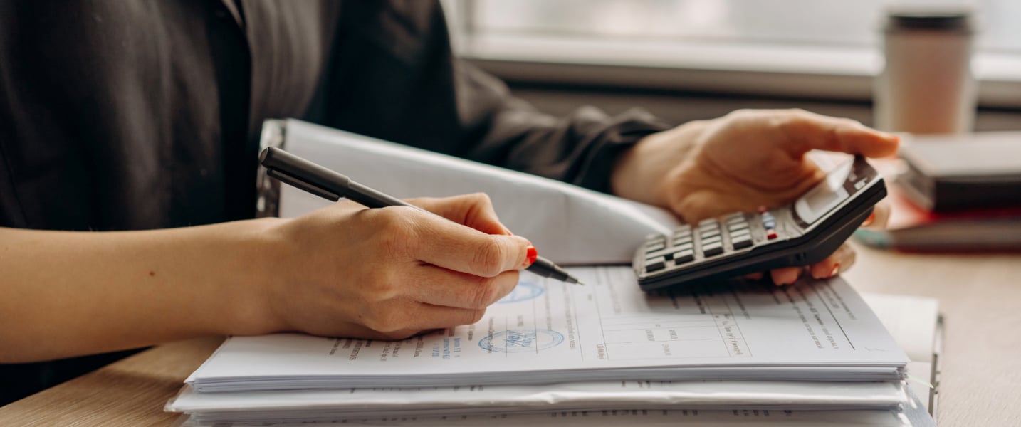  A woman with a focused expression sits at a desk with a calculator and a notepad, deep in thought. This image relates to the idea of outsourcing accounting services in Canada, highlighting the skill and precision required in this field.